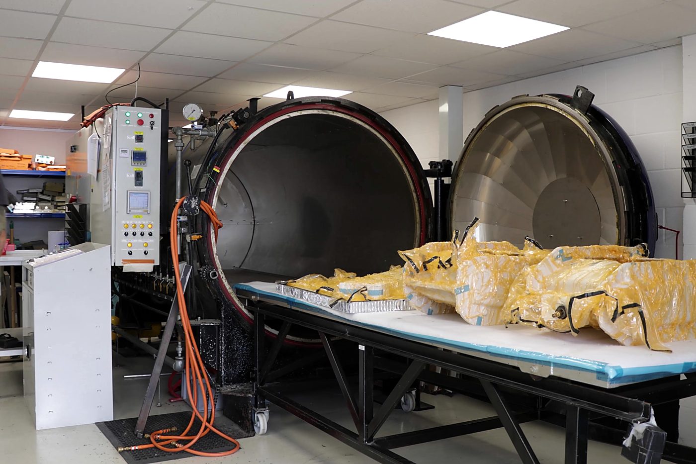Bagged composite parts on a trolley in front of the open autoclave
